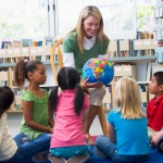 Kindergarten teacher and children looking at globe in library
